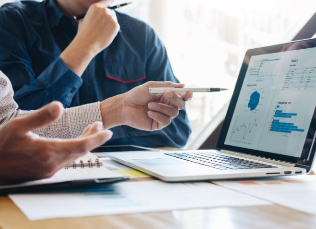 Két ember üzleti megbeszélés közben marketing riportokat elemez egy laptop képernyőjén.